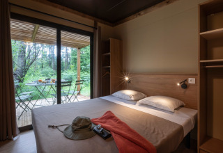 Dormitorio en Chalet Ottawa con cama doble, terraza para desayuno y vista al bosque a través de puertas de cristal.