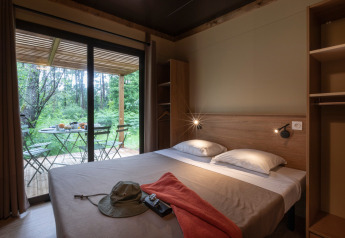 Chambre au Chalet Ottawa avec lit double, terrasse aménagée et vue sur la forêt à travers de grandes baies vitrées.