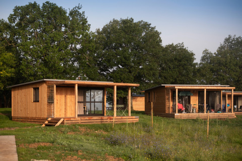 Twee houten chalets bij Chalet Ottawa, Huttopia Pays de Cordes sur Ciel, Frankrijk, met groene bomen.