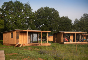 Twee houten hutten bij Chalet Ottawa, Huttopia Pays de Cordes sur Ciel, Frankrijk, met groene bomen.