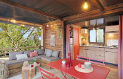 Tienda safari Arizona en Huttopia De Roos con salón, comedor, cocina y vistas al bosque desde la terraza.