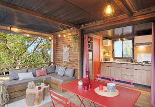 Tienda safari Arizona en Huttopia De Roos con salón, comedor, cocina y vistas al bosque desde la terraza.