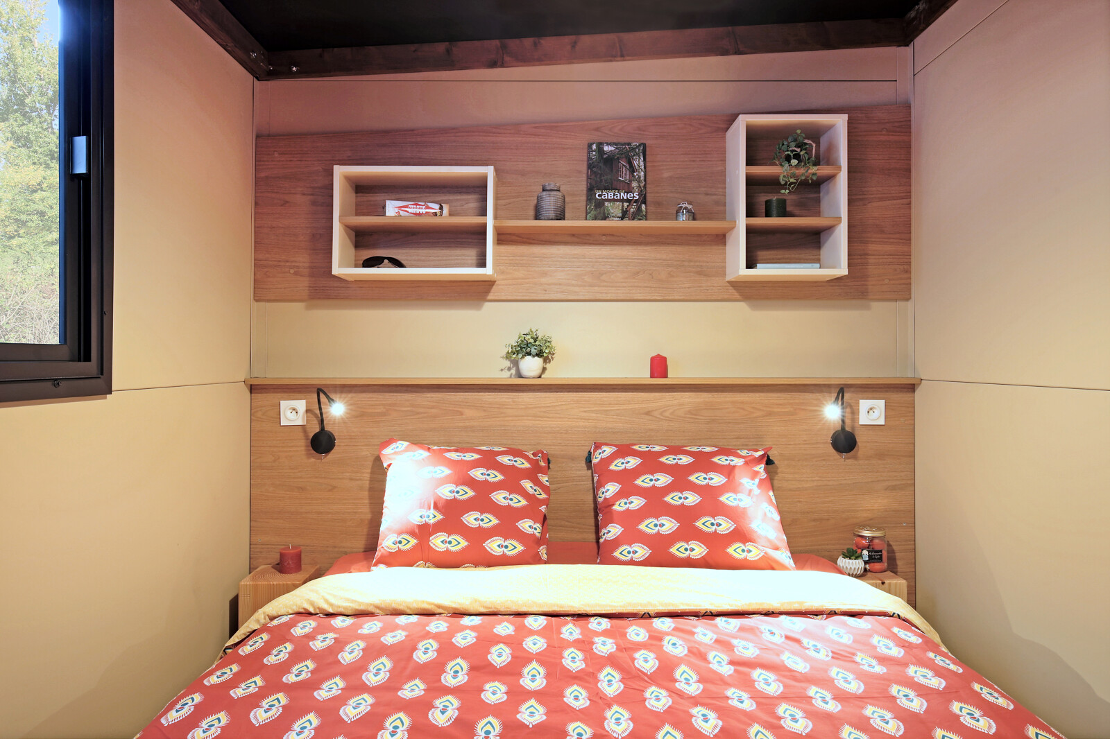Moderne slaapkamer in safaritent Arizona, met houten wanden, planken en rood beddengoed met print.