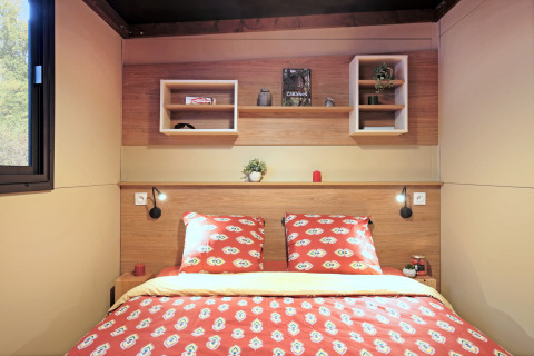 Dormitorio moderno en la tienda safari Arizona, con paneles de madera y ropa de cama roja decorada.