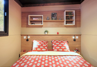 Dormitorio moderno en la tienda safari Arizona, con paneles de madera y ropa de cama roja decorada.