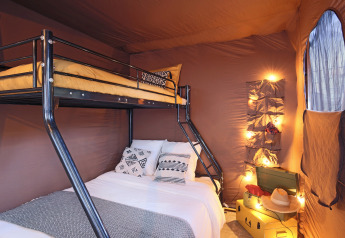 Interior of Arizona safari tent featuring a cozy bunk bed, string lights, and decorative pillows by window.