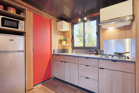 Moderne Küchenzeile im Safari-Zelt Arizona mit Holzfronten, Gasherd, großem Fenster und roter Tür.