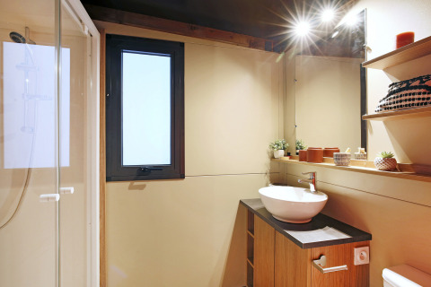 Modernes Badezimmer im Safari-Zelt Arizona mit Dusche, Waschbecken, Fenster und dekorativen Regalen.