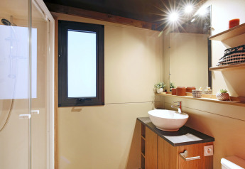 Modernes Badezimmer im Safari-Zelt Arizona mit Dusche, Waschbecken, Fenster und dekorativen Regalen.