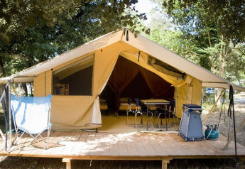 Safari Bungalow tent Classic on wooden deck, surrounded by trees, with chairs, table and camping gear in front.