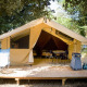 Tienda Safari Bungalow Classic sobre plataforma de madera, con sillas, mesa y equipo de camping, rodeada de árboles.
