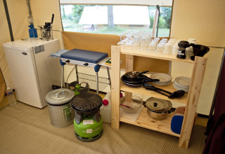 Goed uitgeruste campingkeuken met koelkast, fornuis, borden en glazen in een safaritent bungalow in Frankrijk.
