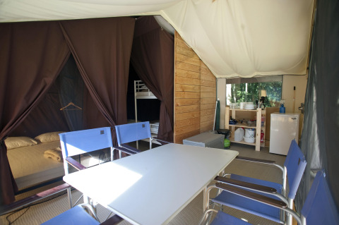 Vista interior de la tienda safari Toile&Bois Sweet con mesa, sillas, cama, zona de cocina y nevera.