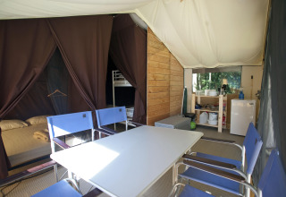 Vista interior de la tienda safari Toile&Bois Sweet con mesa, sillas, cama, zona de cocina y nevera.