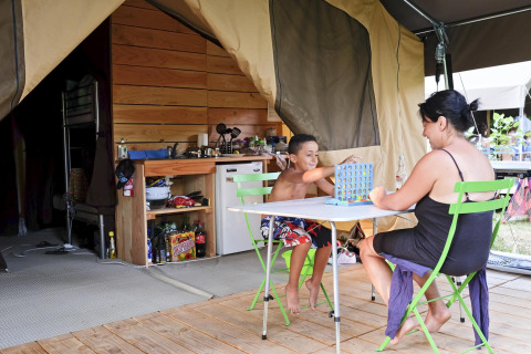 Madre e figlio giocano a un gioco da tavolo davanti a una tenda safari a Huttopia Lac de Carcans, Francia.