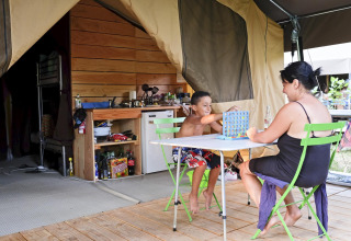 Moeder en zoon spelen een gezelschapsspel aan een tafel voor een safaritent bij Huttopia Lac de Carcans, Frankrijk.