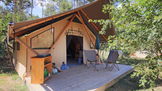 Tienda safari Trappeur Tent con terraza de madera, dos sillas, sombrilla y armario en entorno natural.