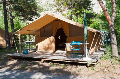 Tienda safari Trappeur sobre terraza de madera en Huttopia Gorges du Verdon, Francia, entre árboles verdes.