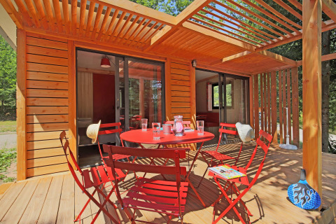 Terraza en Chalet Ottawa, Huttopia Baie du Mont St Michel, Francia, con sillas rojas y pérgola de madera.