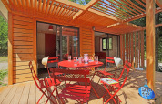 Terraza en Chalet Ottawa, Huttopia Baie du Mont St Michel, Francia, con sillas rojas y pérgola de madera.