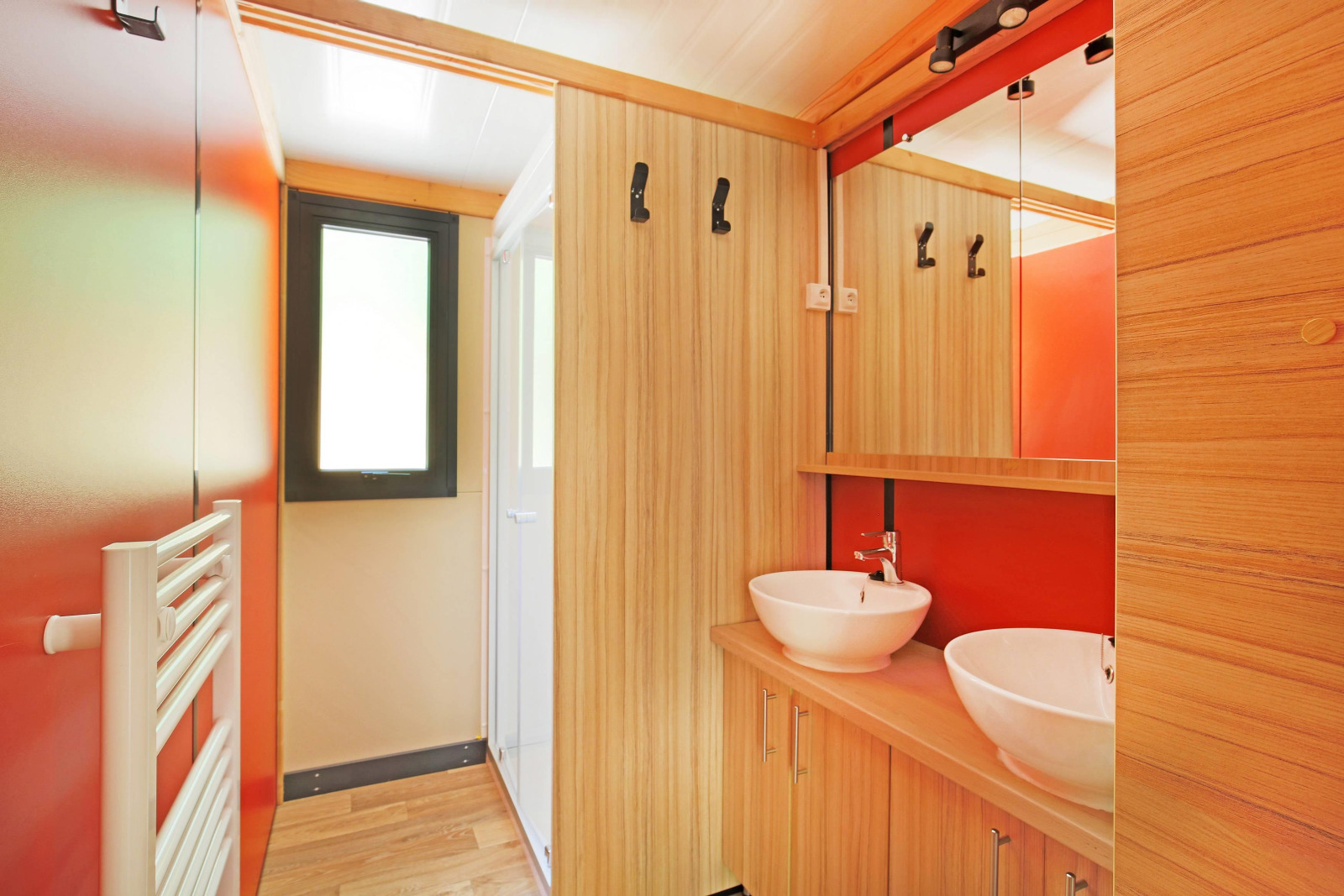 Moderne badkamer met dubbele waskom, houten afwerking en rode accenten in Chalet Ottawa, Huttopia Baie du Mont St Michel.