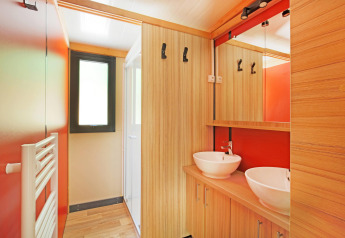 Moderne badeværelse med dobbelt håndvask, træelementer og rød væg i Chalet Ottawa, Huttopia Baie du Mont St Michel.