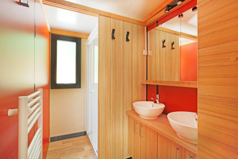 Baño moderno con dos lavabos de tipo bol, acabados de madera y paredes rojas en Chalet Ottawa, Huttopia Baie du Mont St Michel.