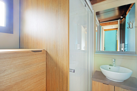 Helles Badezimmer mit Holzverkleidung, runder Waschschüssel und Spiegel in Chalet Evasion bei Huttopia Baie du Mont St Michel.