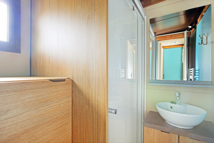 Salle de bain lumineuse avec bois, vasque ronde et grand miroir au Chalet Evasion à Huttopia Baie du Mont St Michel.
