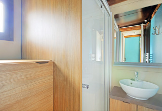 Helles Badezimmer mit Holzverkleidung, runder Waschschüssel und Spiegel in Chalet Evasion bei Huttopia Baie du Mont St Michel.