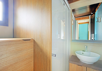 Bagno luminoso con pareti in legno, lavabo rotondo e grande specchio nel Chalet Evasion a Huttopia Baie du Mont St Michel.