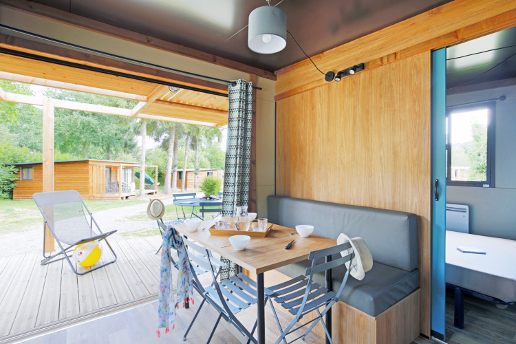 Vue intérieure d’un chalet confortable à Huttopia Baie du Mont St Michel, avec terrasse et cabanes boisées.