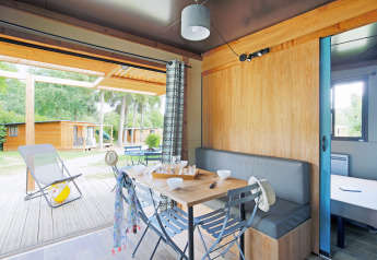 Vista interior de un chalet acogedor en Huttopia Baie du Mont St Michel, con terraza y cabañas afuera.
