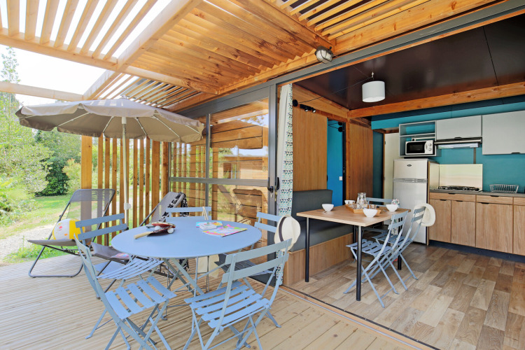 Terrasse couverte et cuisine moderne dans l’hébergement glamping Chalet Evasion au décor en bois.
