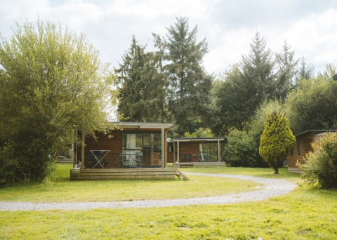 Chalet Evasion bei Huttopia Baie du Mont St Michel in Frankreich, umgeben von grüner, bewaldeter Landschaft.