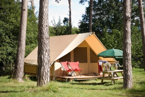 Safari-Zelt Canadienne auf Huttopia Rambouillet in Frankreich, umgeben von Bäumen und Sitzgelegenheiten.