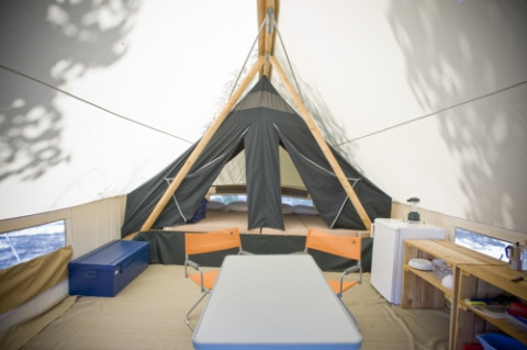 Interior de tienda safari Canadienne en Huttopia Rambouillet, con mesa, sillas y cama en el fondo.