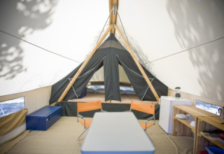 Innenansicht eines Canadienne-Safari-Zeltes bei Huttopia Rambouillet mit Tisch, Stühlen und Bett.