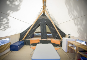Innenansicht eines Canadienne-Safari-Zeltes bei Huttopia Rambouillet mit Tisch, Stühlen und Bett.