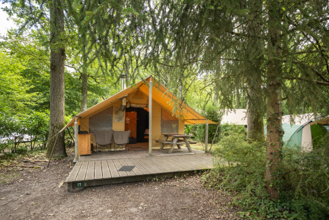 Tenda safari Tente Trappeur con veranda in legno, tavolo da picnic e sedie in un campeggio nel bosco.