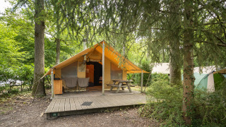 Tenda safari Tente Trappeur con veranda in legno, tavolo da picnic e sedie in un campeggio nel bosco.