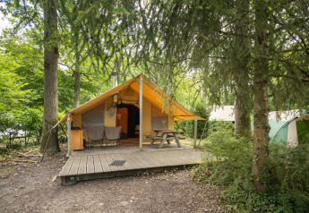 Safari tent Tente Trappeur with front deck, picnic table and chairs, set in a scenic wooded campsite.