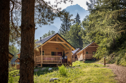 Træhytter ved Chalet Montana omgivet af skov og bjerge, fredelig naturferie i alperne om sommeren.