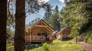 Træhytter ved Chalet Montana omgivet af skov og bjerge, fredelig naturferie i alperne om sommeren.