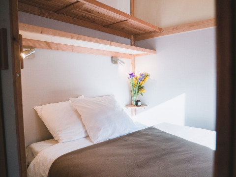 Cama acogedora con sábanas blancas y flores en Chalet Montana de Huttopia Bozel en Vanoise, Francia.