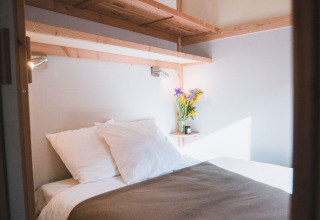 Cama acogedora con sábanas blancas y flores en Chalet Montana de Huttopia Bozel en Vanoise, Francia.