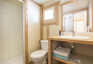 Lyst og hyggeligt badeværelse med trædetaljer i Chalet Montana ved Huttopia Bozel en Vanoise, Frankrig.