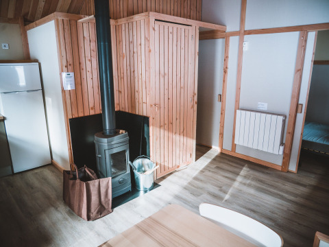 Interior del Chalet Montana en Huttopia Bozel en Vanoise, Francia, con estufa de leña y paredes de madera.
