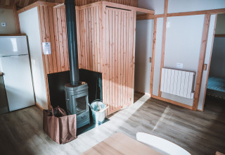 Interior del Chalet Montana en Huttopia Bozel en Vanoise, Francia, con estufa de leña y paredes de madera.
