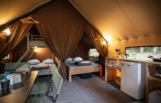 Interior view of a safari tent featuring beds, a small kitchen area, and a dining table for guests.